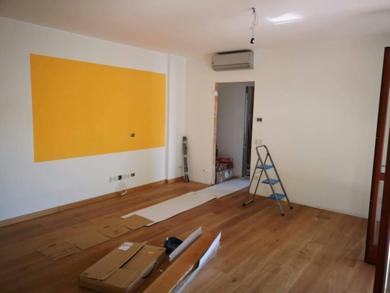 A bright, empty room under renovation with ladder, tools, and wooden flooring.