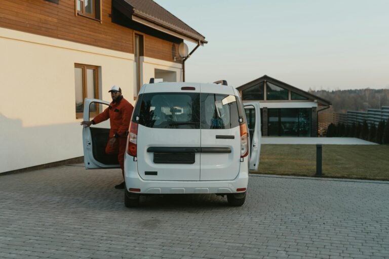 A worker in uniform exits a white van parked in a residential driveway during daytime.